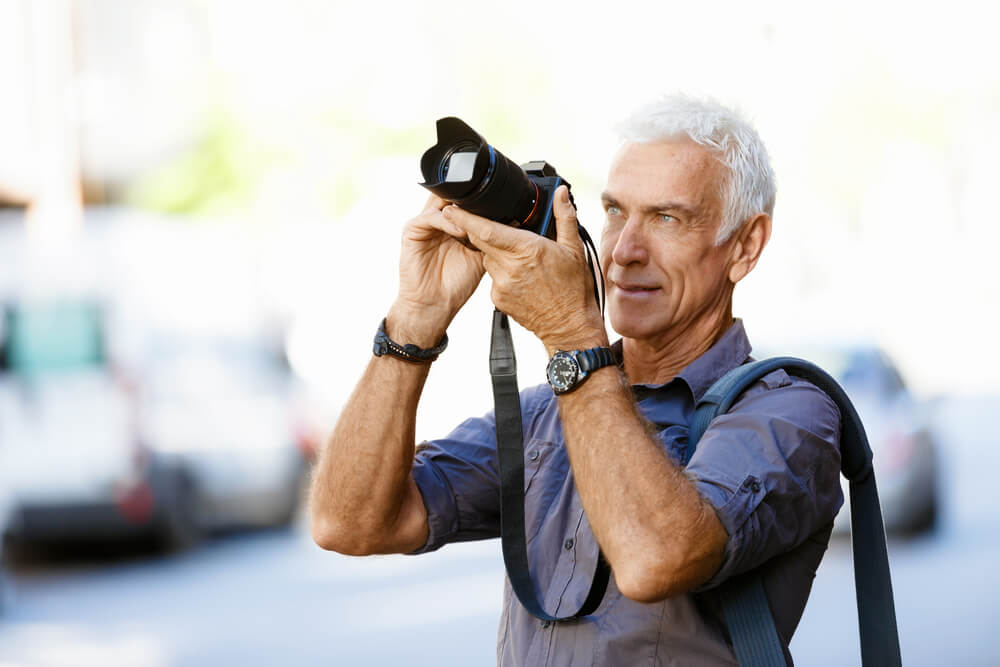 Older man holding a camera outside